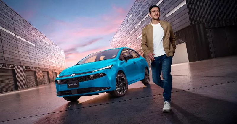 Foto del nuevo Nissan Versa 2026 estacionado entre dos edificios y con un joven caminando a su lado.