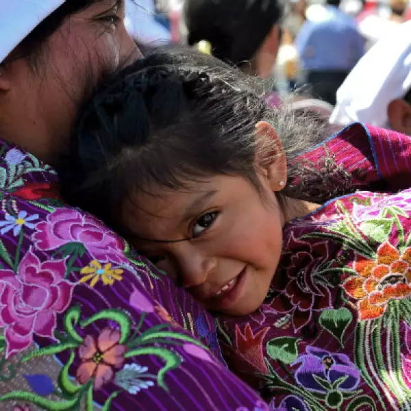Una pequeña se refugia del sol en los brazos de su madre.