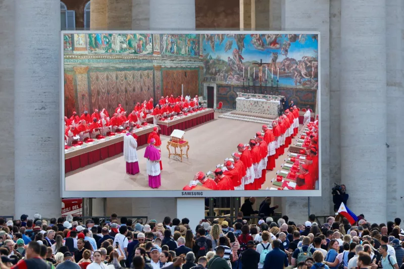 La gente mira una pantalla en la Plaza de San Pedro que muestra a los cardenales en la Capilla Sixtina, el primer día del cónclave para elegir al siguiente Papa, visto desde Roma, Italia, el 7 de mayo de 2025.