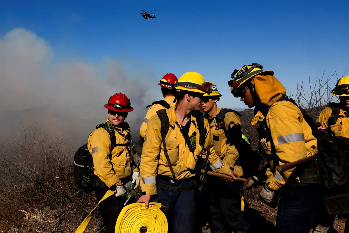 ILos bomberos del Departamento de Bomberos del Condado de Los Ángeles se reúnen mientras un helicóptero vuela, mientras el incendio de Palisades continúa en el Cañón de Mandeville, en Los Ángeles, California, EE. UU., 11 de enero de 2025