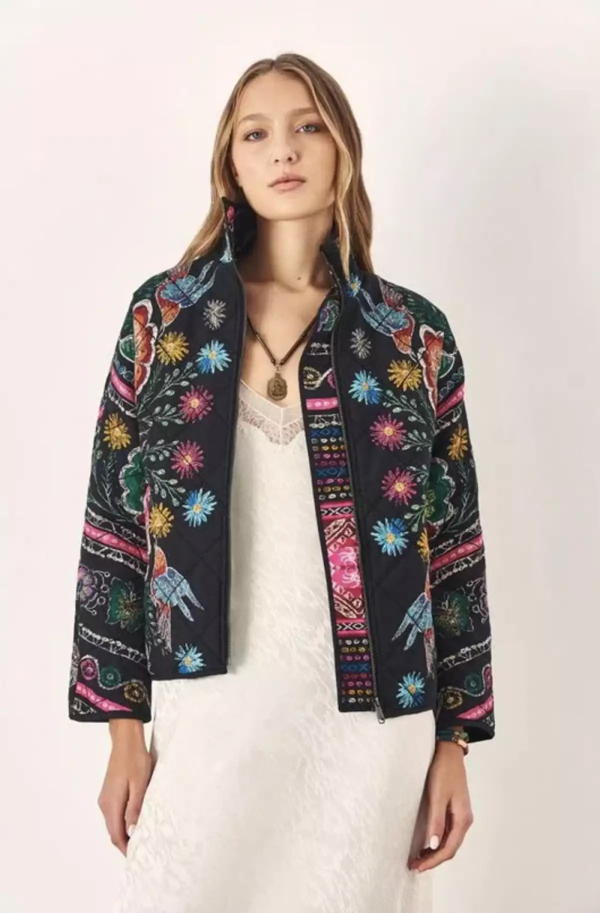 modelo con vestido blanco y una chamarra multicolor de Rapsodia. 