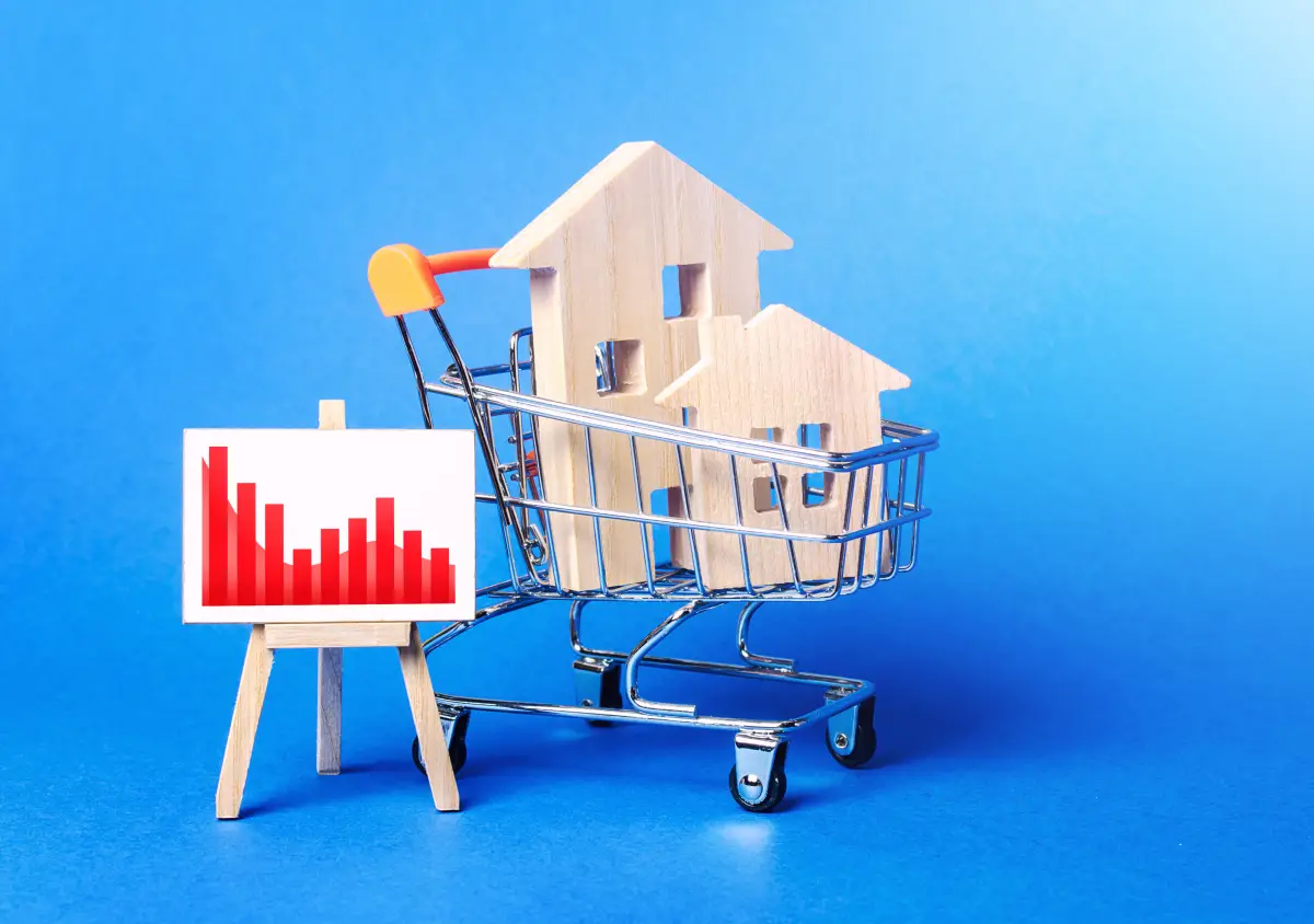 Wooden houses in a shopping cart and an easel with a red negative falling trend chart. Low sales. Value cost decrease. Bad attractiveness. Real estate market fall. Cheap rent. Reduced demand